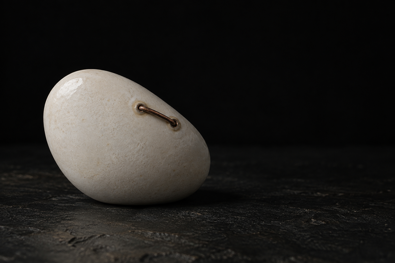 An intact pale ceramic object bearing a conspicuous copper intervention on its smooth unbroken surface.